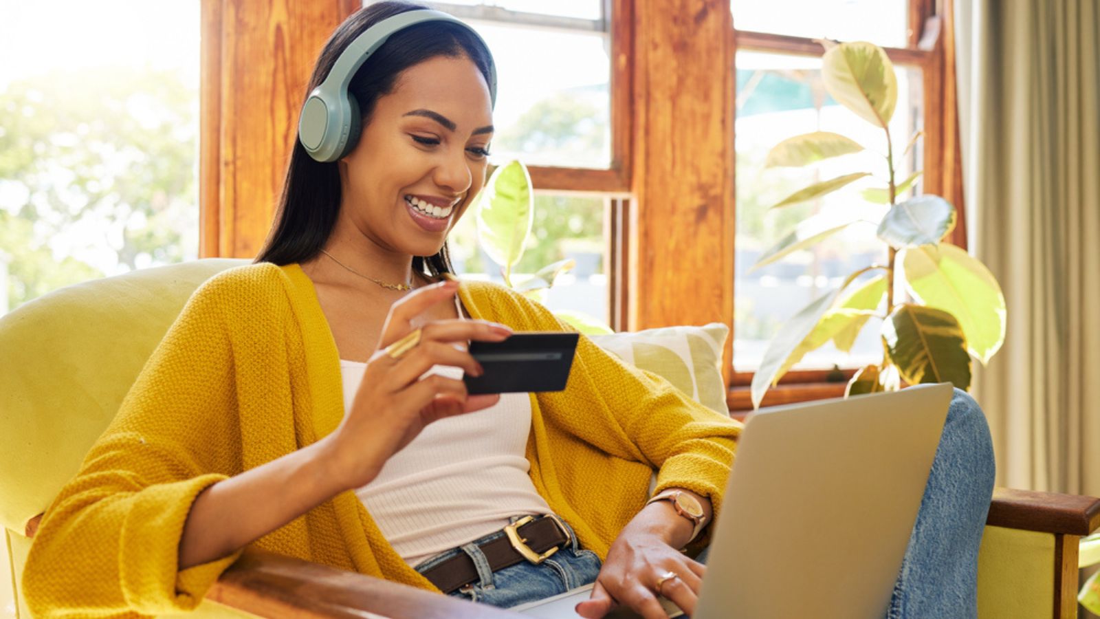 Woman in yellow with headphones spending money on her credit card at her computer