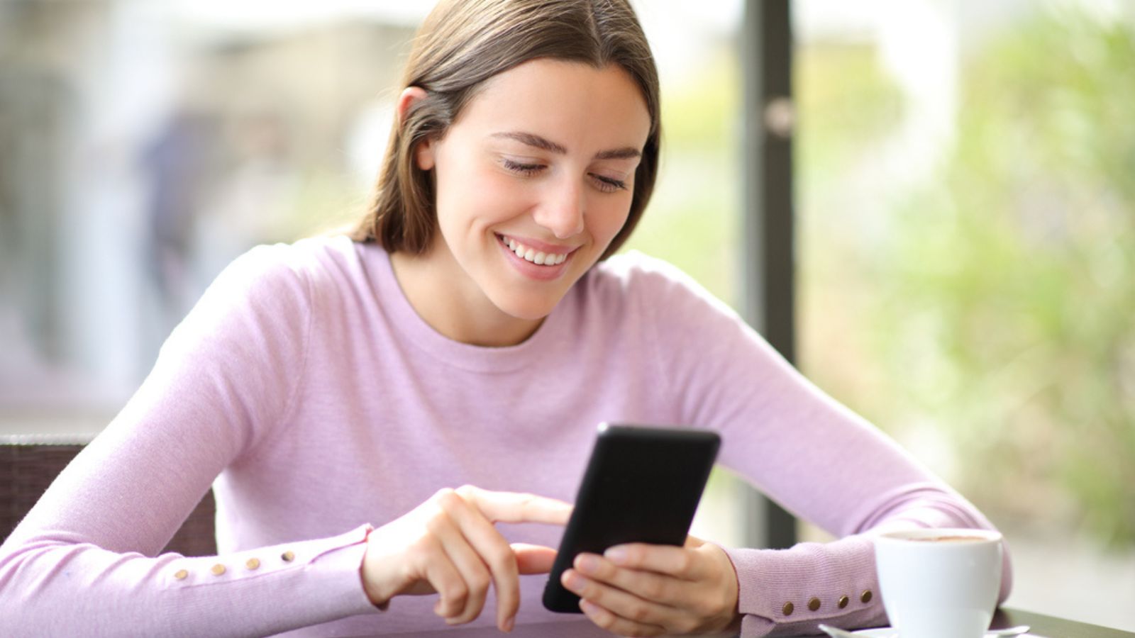 Happy woman using mobile phone checking online content sitting in a coffee shop