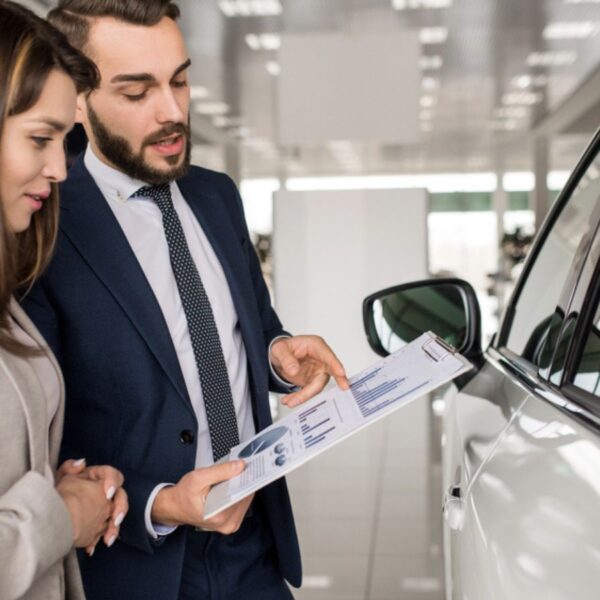 Side view portrait of modern young woman listening to car dealer while choosing luxury car in showroom