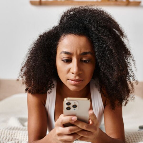 woman on her cell phone lying on a bed curly afro hair