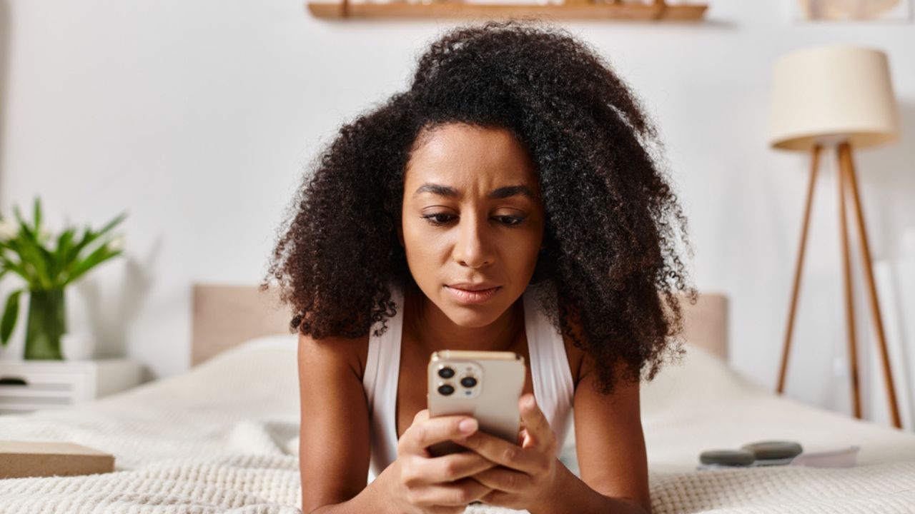 woman on her cell phone lying on a bed curly afro hair