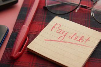 a note that says pay debt next to a pen and glasses; debt after job loss