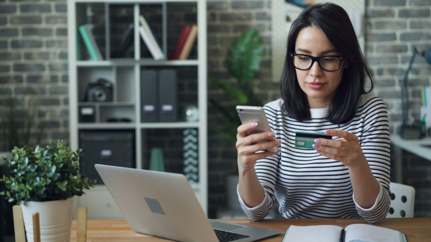 a woman sitting at a table looking at her cell phone; credit cards