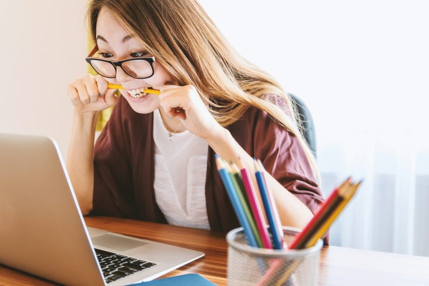woman biting pencil while sitting on chair in front of computer during daytime; refinance your student loans