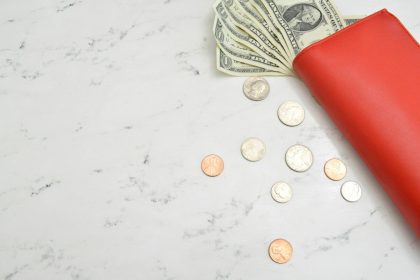 fan of 1 US dollar banknotes and coins on beige surface; debt avalanche vs. debt snowball
