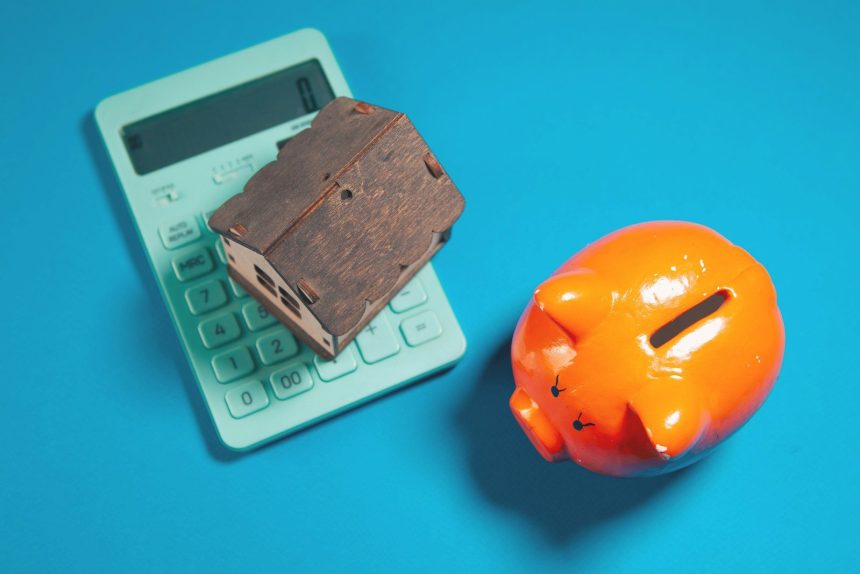 Calculator, piggy bank, and house model on blue background; building a budget