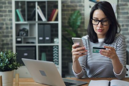 a woman sitting at a table looking at her cell phone; credit card mistakes
