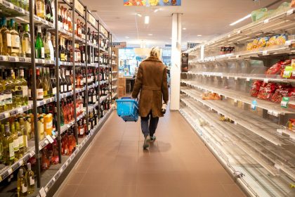 woman in brown coat walking on hallway; how to save money on groceries