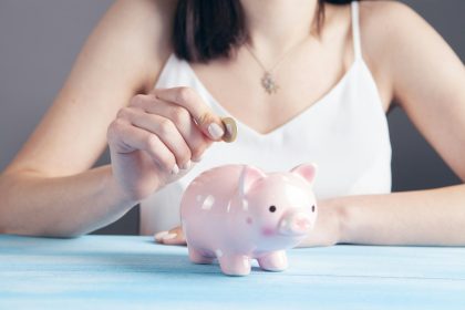 woman in white tank top holding pink pig figurine; save for retirement