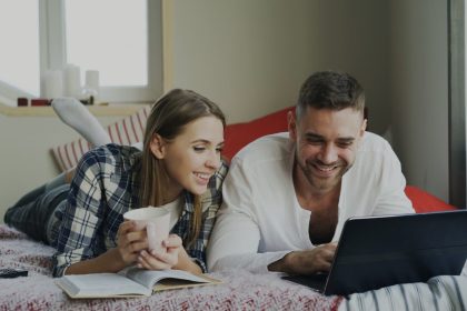 Couple lying on bed with laptop and coffee; budgeting as a couple
