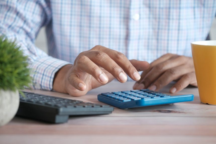person using calculator at desk with coffee mug; debt payoff mistakes