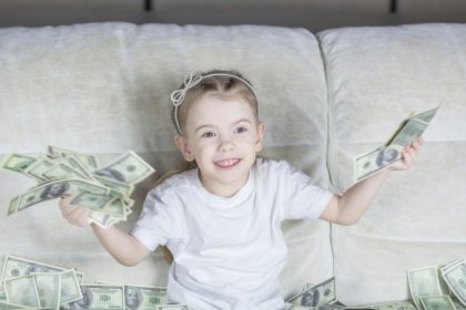 a little girl sitting on a couch holding money; teaching kids about money