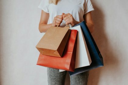 Woman holding shopping bags in front of white wall; buy now pay later