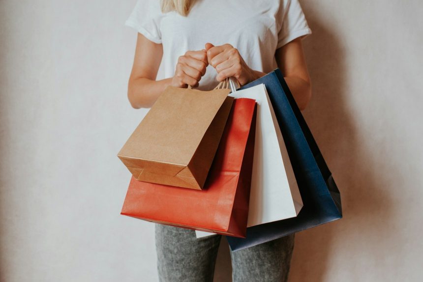 Woman holding shopping bags in front of white wall; buy now pay later