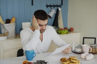 Man sitting at table reading papers with breakfast; AI debt collectors