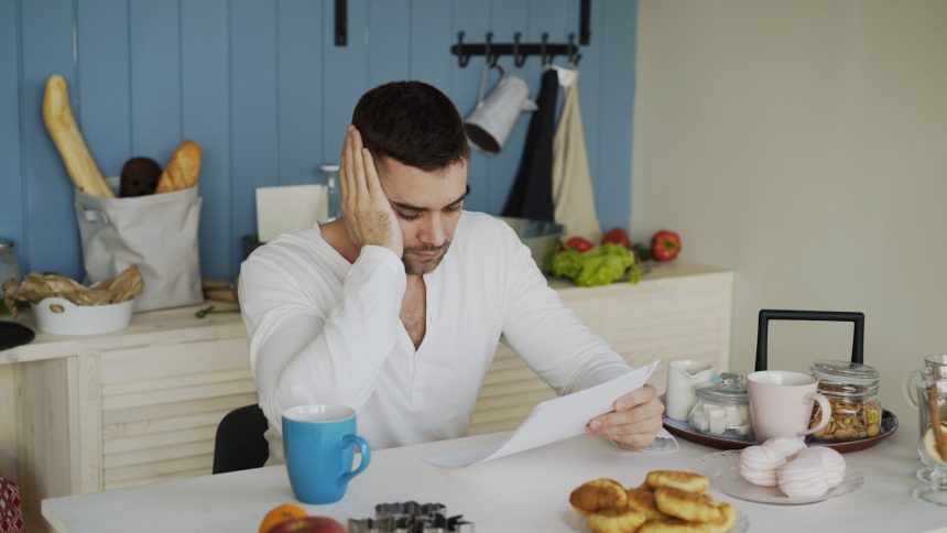 Man sitting at table reading papers with breakfast; AI debt collectors