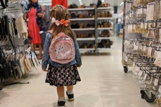 girl in pink and blue floral dress standing on white floor tiles; back to school debt