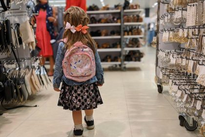 girl in pink and blue floral dress standing on white floor tiles; back to school debt