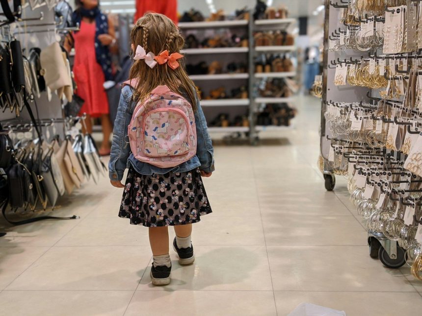 girl in pink and blue floral dress standing on white floor tiles; back to school debt