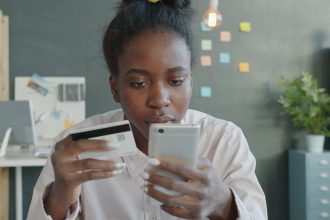 Woman holding credit card and smartphone for online shopping.; credit card debt