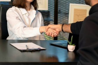 a man and a woman shaking hands in front of a laptop; negotiate your salary