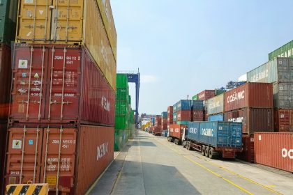 a long line of shipping containers on the side of a road; tariffs