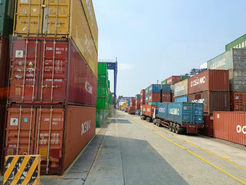 a long line of shipping containers on the side of a road; tariffs