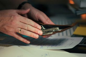Hands holding cash in a wallet over papers; personal loan debt