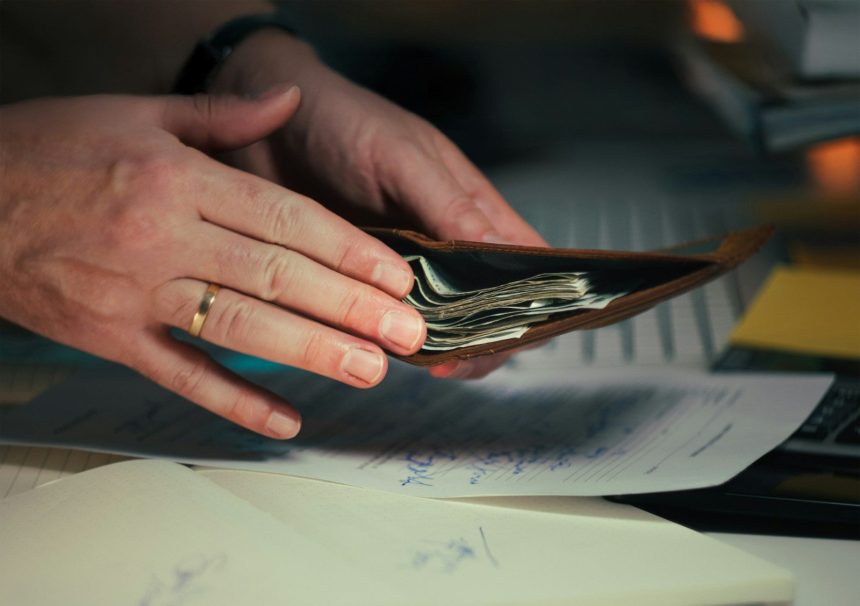 Hands holding cash in a wallet over papers; personal loan debt
