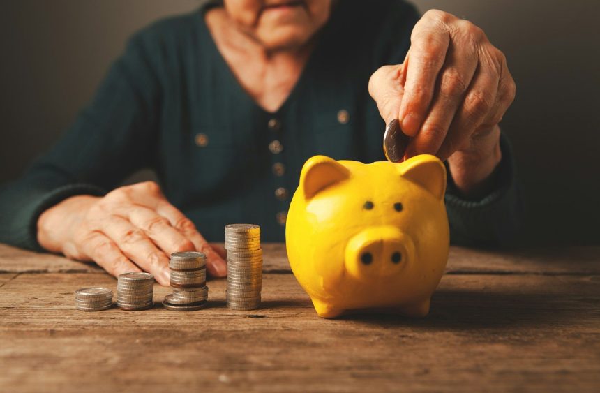 Elderly hands depositing coins into a yellow piggy bank; retirement debt