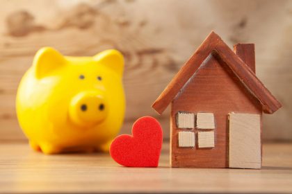 Yellow piggy bank with wooden house and red heart; Parent PLUS loan debt