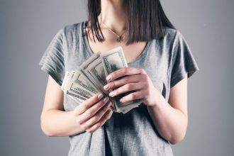 woman in gray shirt holding fan of us dollar bills; Gen Z debt